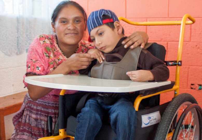 Angel in his new wheelchair and his mother, Eusebia, next to him smiling at the camera.