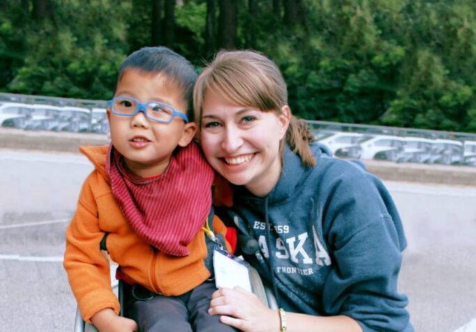 A picture of a little boy with glasses on, smiling, with his Joni and Friends buddy next to him.