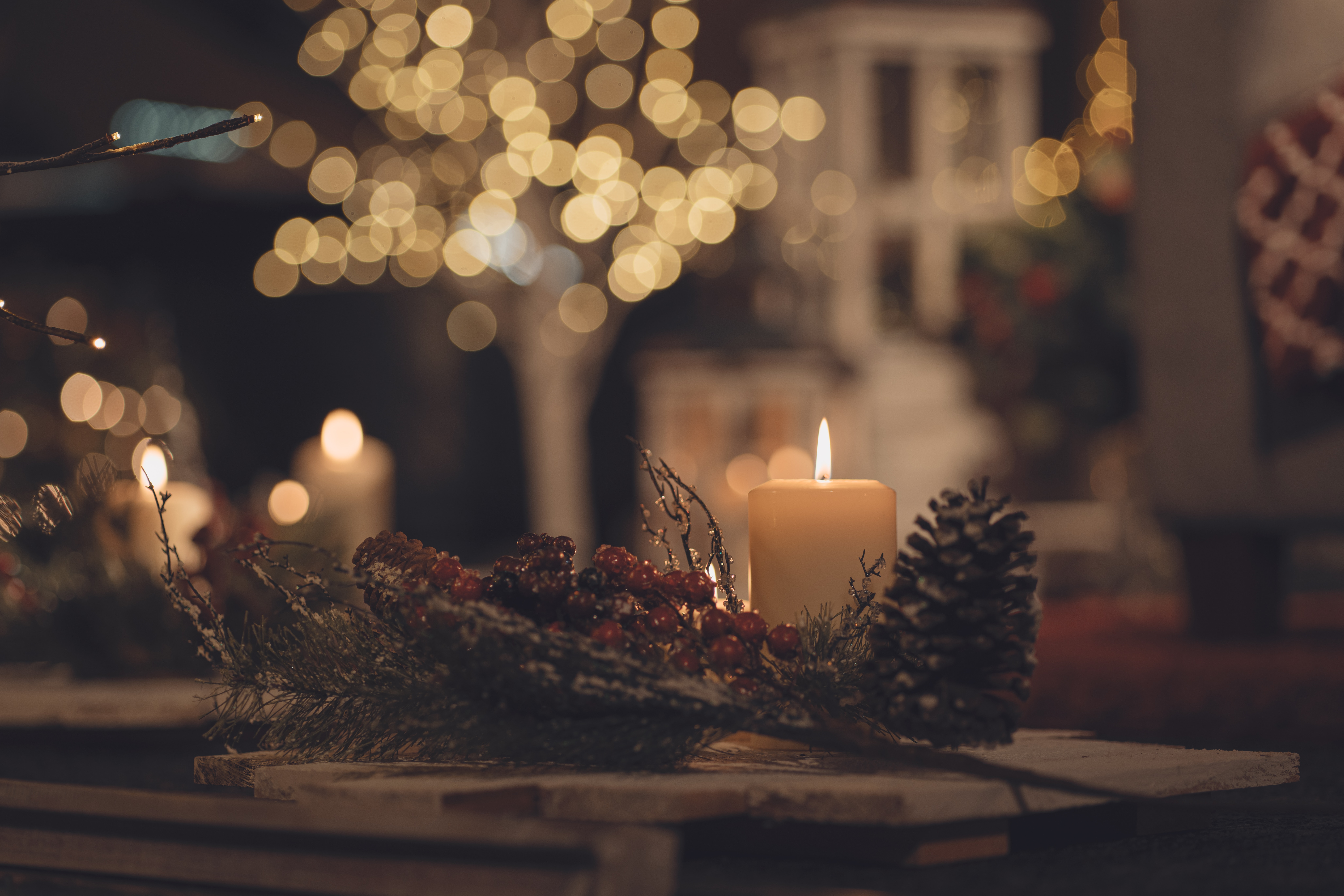 A lit candle sitting on a table with tree sprigs, holly, and a pinecone surrounding it.
