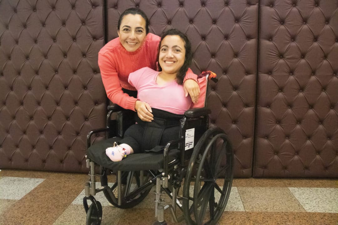 A mother and child posing for a photo. The child is smiling in her new wheelchair