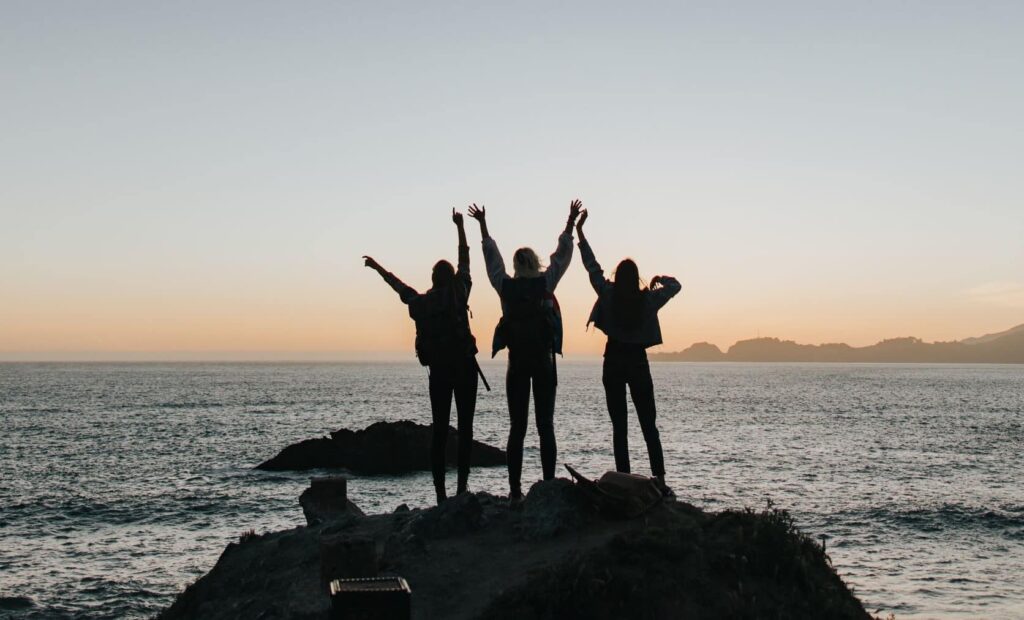 A silhouette of three people raising their hands by a body of water