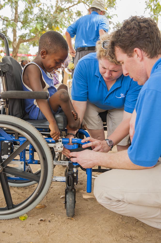 A boy watches as volunteers fix his wheelchair