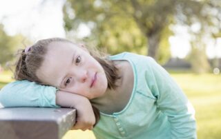 A childhood photo of Sarah Amick, daughter of Shauna, a girl with Down syndrome resting her head on a table and looking at the camera.