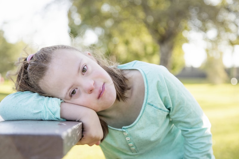 A childhood photo of Sarah Amick, daughter of Shauna, a girl with Down syndrome resting her head on a table and looking at the camera.