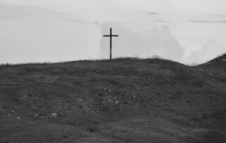 A black and white photo of a cross on a hill.