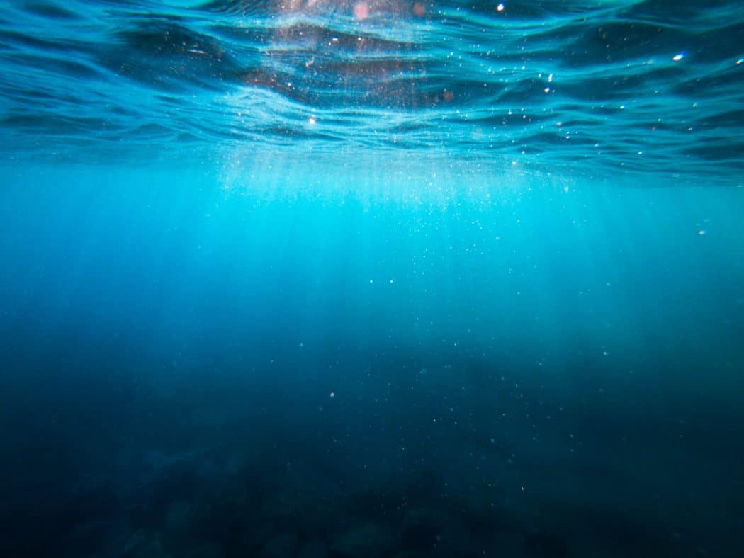 Close up of the ocean from beneath the surface as the light is shining through the water.