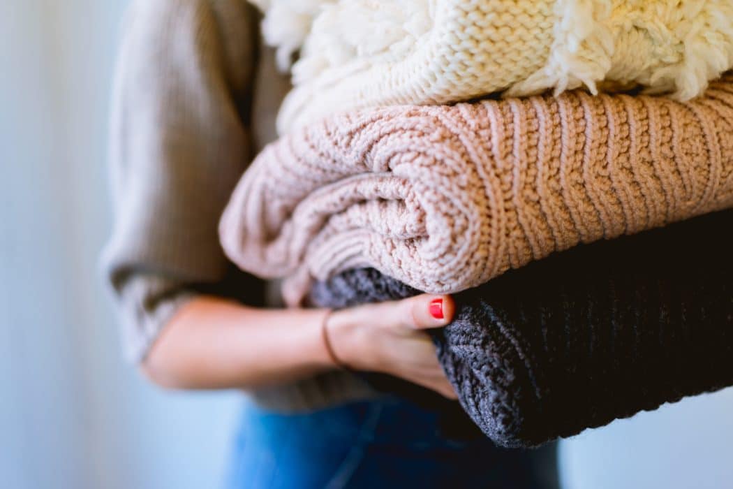 A woman holding a stack of thick knitted blankets.
