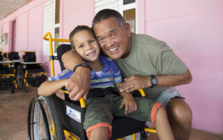 A child in his new wheelchair takes a picture with Ken Tada