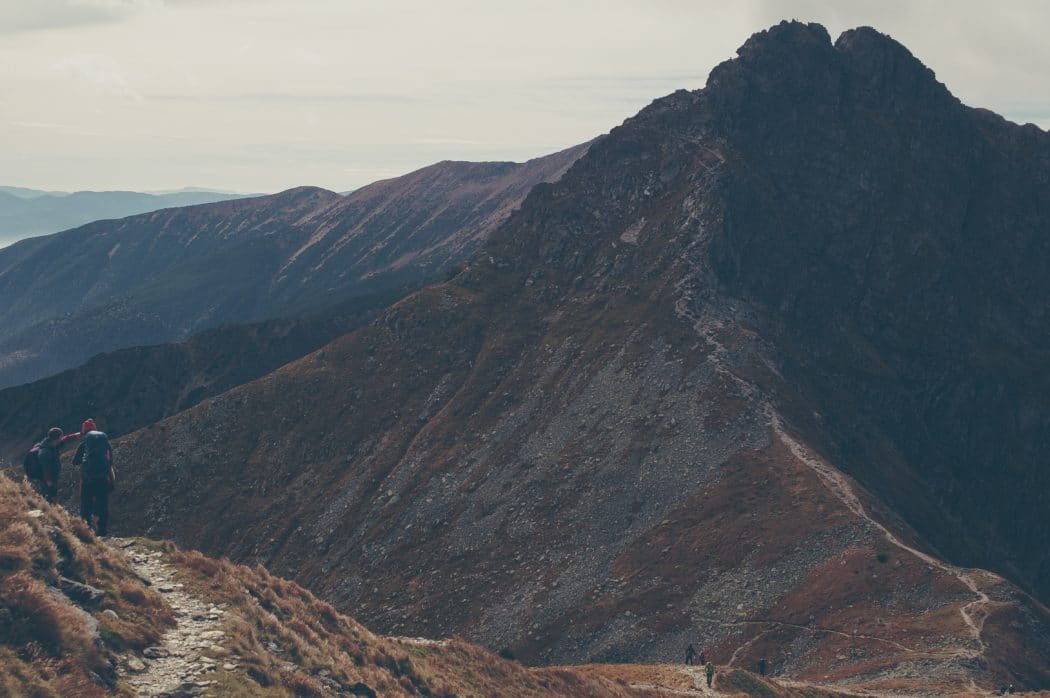 Two men hiking on a path along a mountain and pointing at another mountain range next to them.
