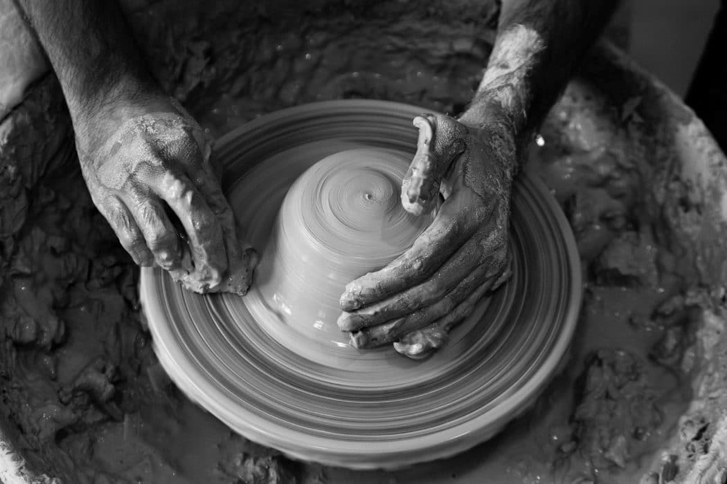 Close up of a man working clay on a spinning wheel.