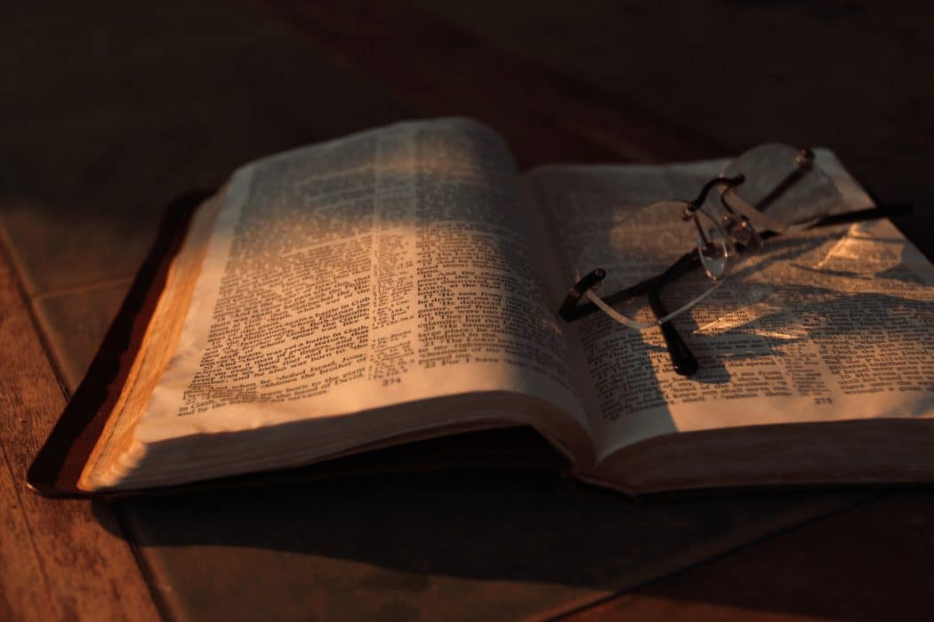 A bible sitting open on a wooden table with reading glasses sitting on it.
