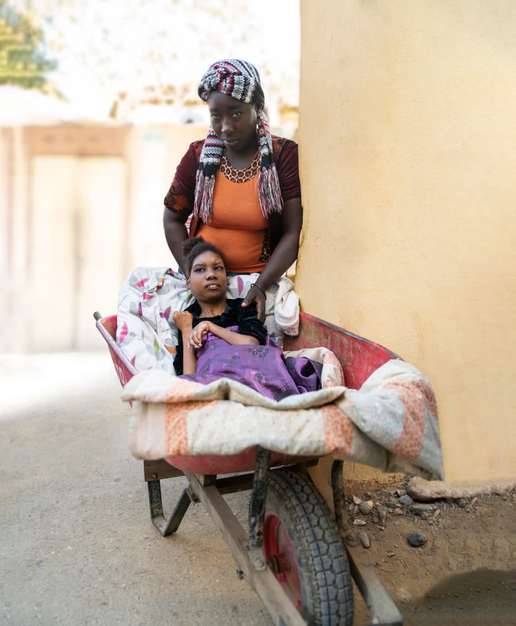 Josleen in a wheelbarrow and her mom standing behind her. 