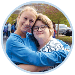 A young Joni and Friends voltuneer hugging a young girl with down-syndrome as they both smile at the camera.