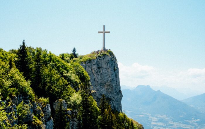 A cross on top of a beautiful green cliffside and hills in the distance.