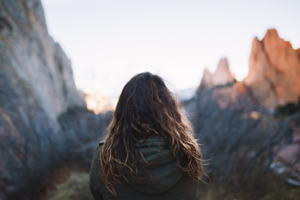 A picture from behind a woman as she looks out at a beautiful mountain range.