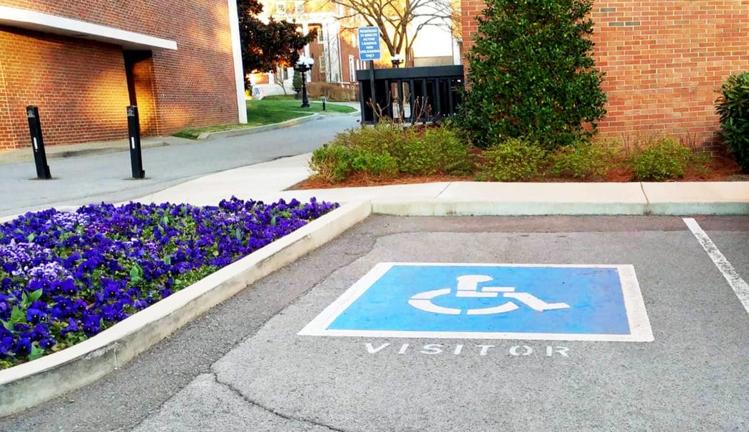 Close up of a handicap parking spot with flowers in a planter next to it and brick buildings behind it.