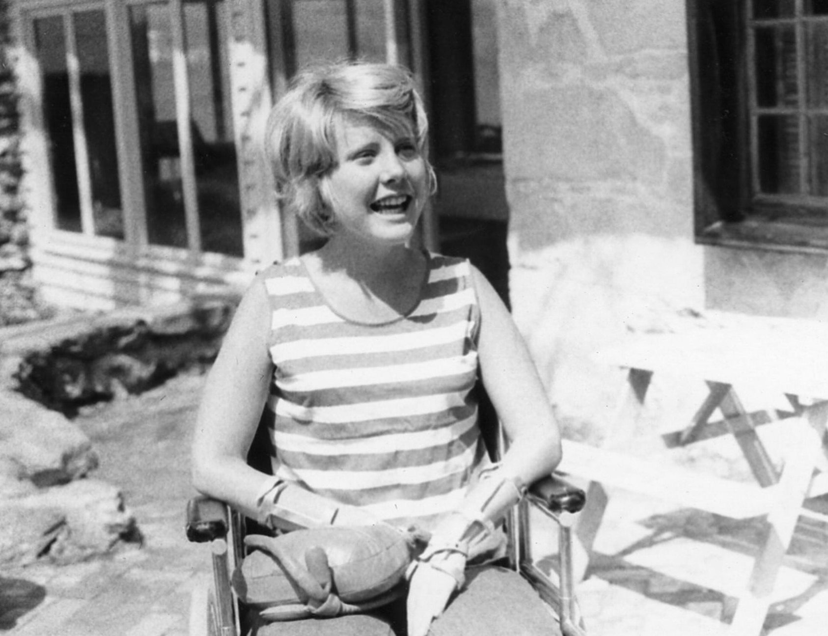 Young Joni sits in her wheelchair and is looking past the camera smiling.