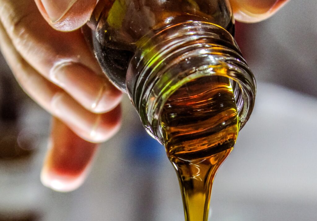 A close-up of a hand pouring a thick, golden-amber liquid from a glass bottle.