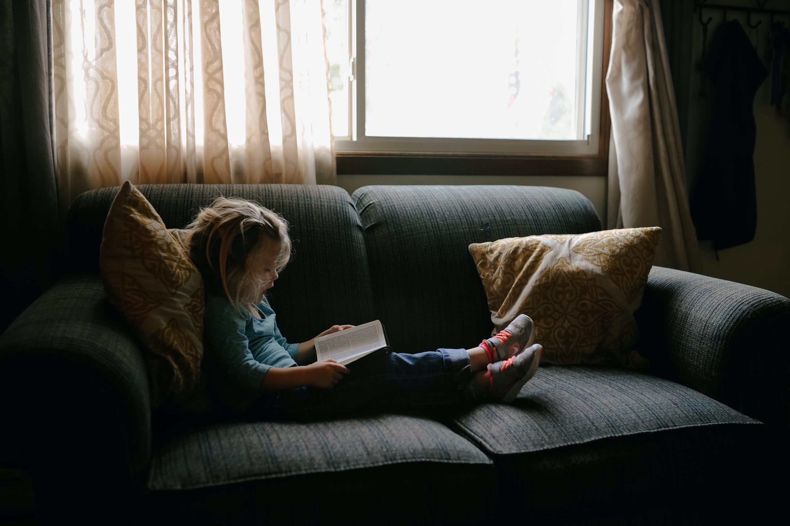 A little girl reading her bible on the couch.