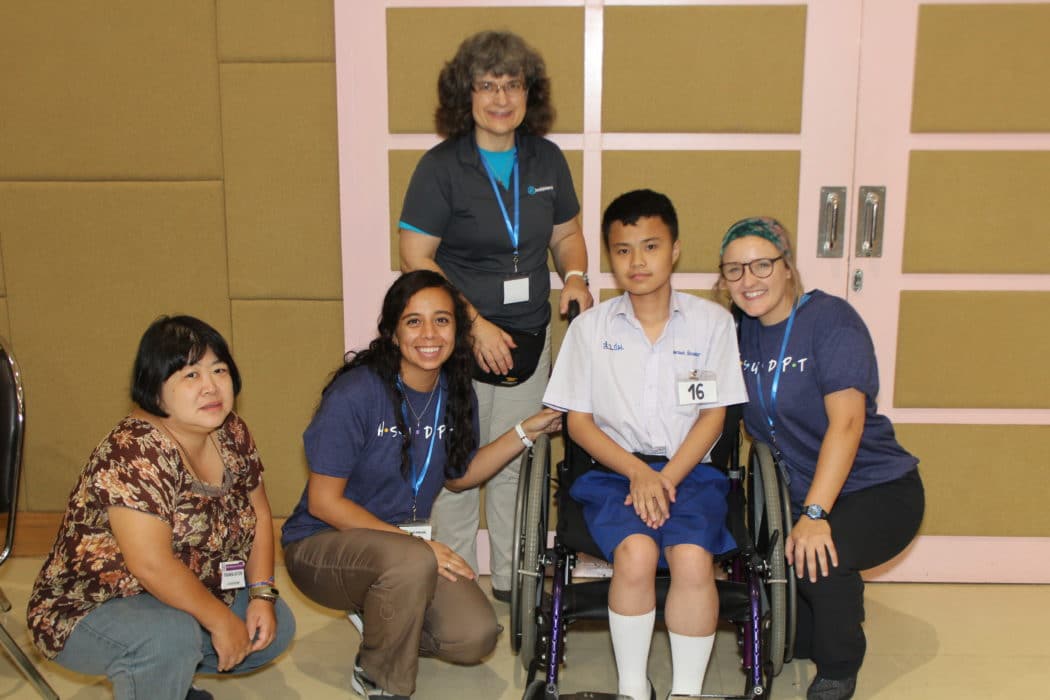A scene of Joni and Friends volunteers kneeling next to a mother and her son who is seated in his wheelchair.
