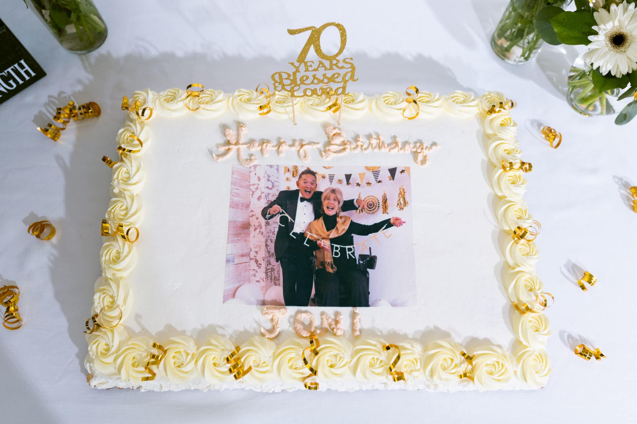 Close up of a birthday cake with an image of Joni and Ken holding a sign that says "celebrate" on it.