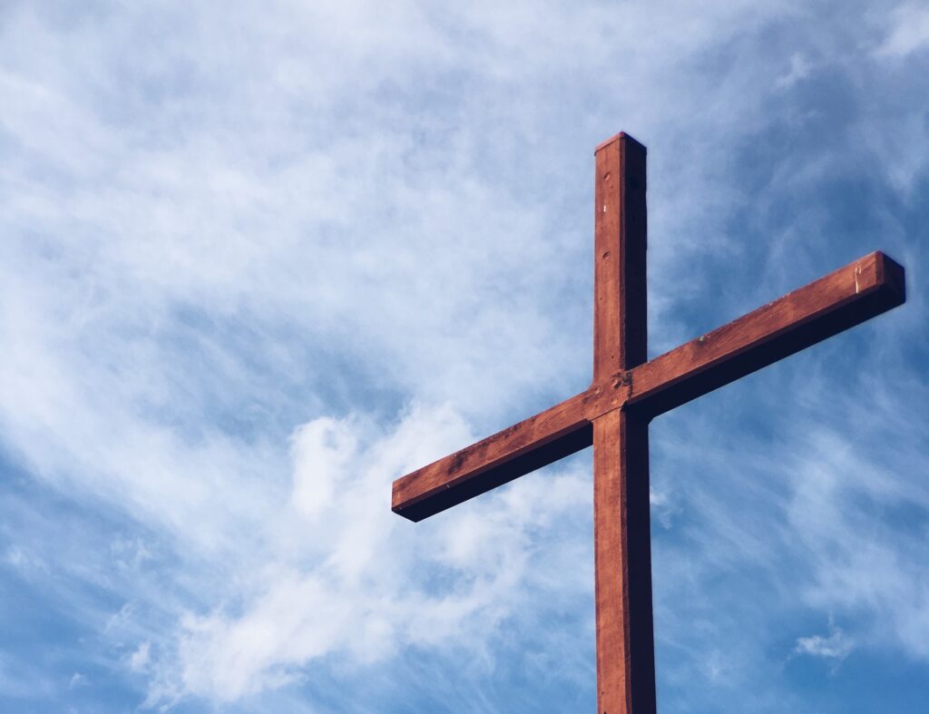 Close up of a wooden cross with a blue sky behind it.