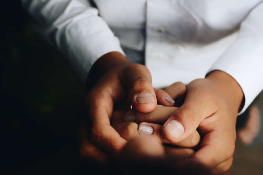 Close up of a man in a button down shirt holding a woman's hands in his.