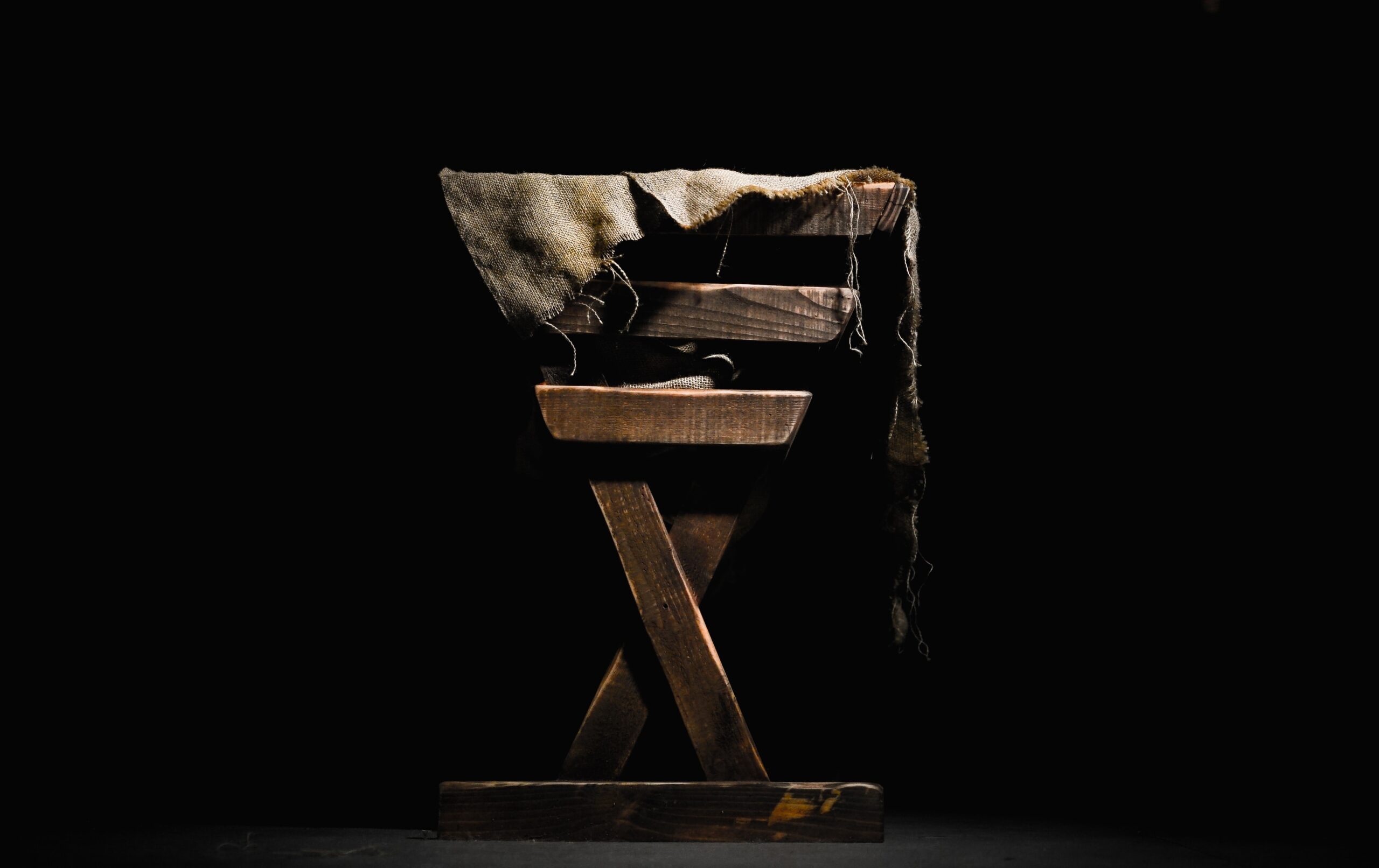 A wooden manger with rags in it and a black background.