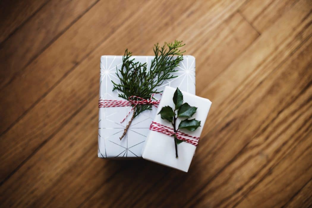 A Christmas gift on a wooden table, wrapped with shiny paper and tree branches attached with ribbon.