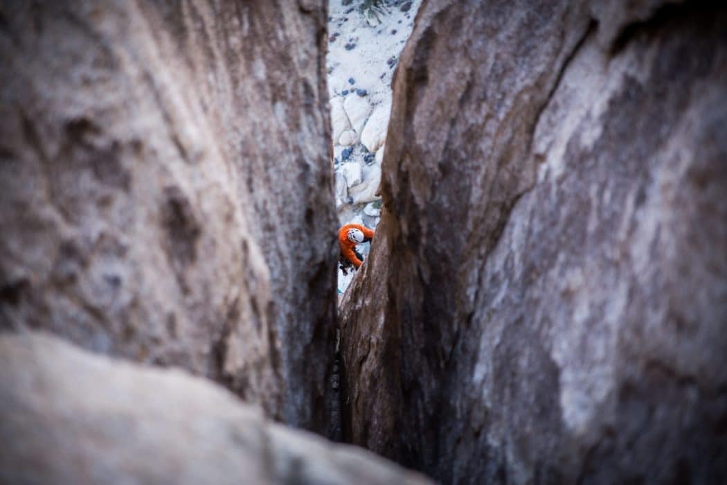 A close up of a climber making his way up the side of a mountain.