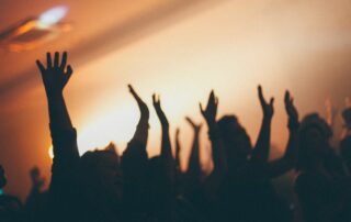 A picture of people in a worship center raising their hands in worship.