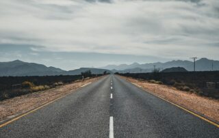 A picture of an empty road running towards a mountain range with grey clouds above.