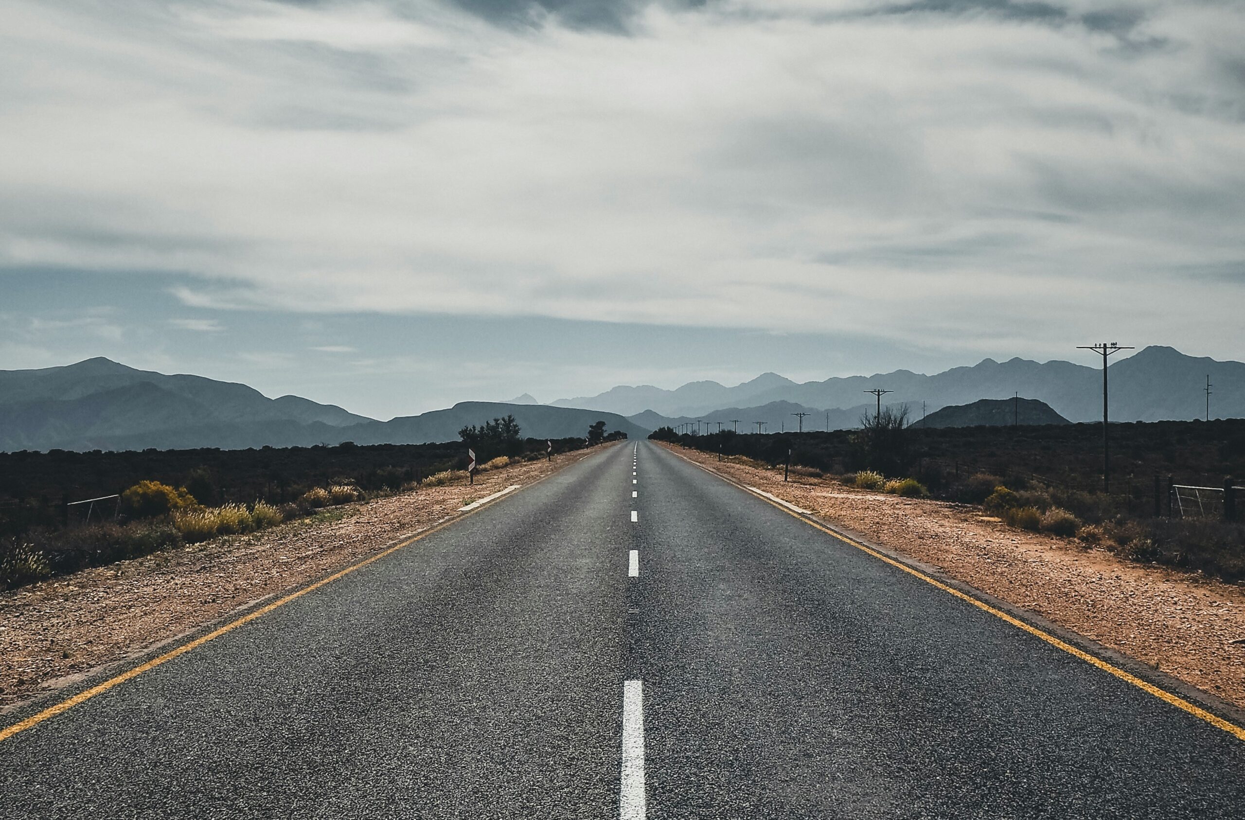 A picture of an empty road running towards a mountain range with grey clouds above.