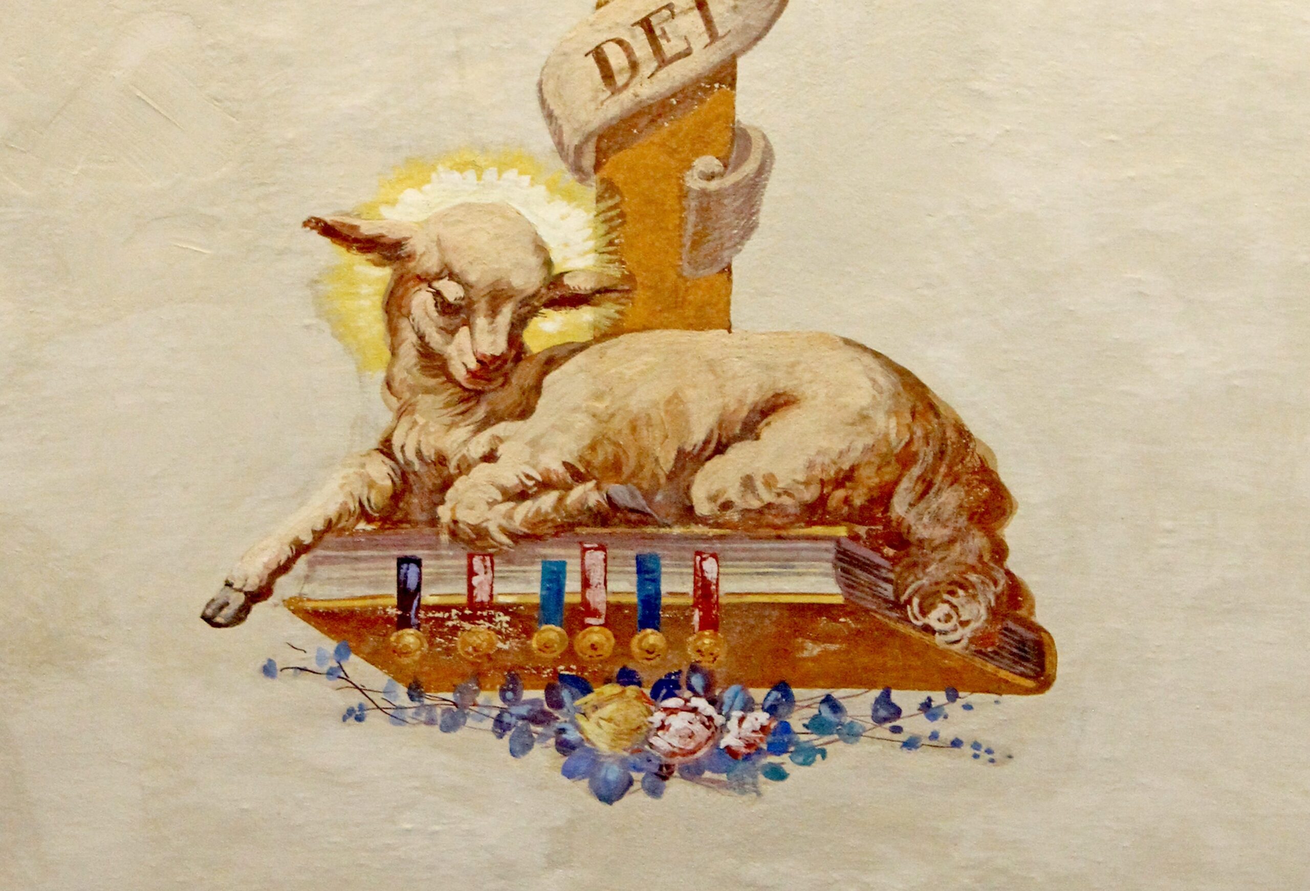 Close up of the icon of the Lamb of God seated on a book with flowers beneath it and a heavenly glow around its head.