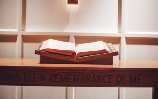 A picture of a Bible laid out on an altar. The phrase, "This do in remembrance of me," engraved in the wood.