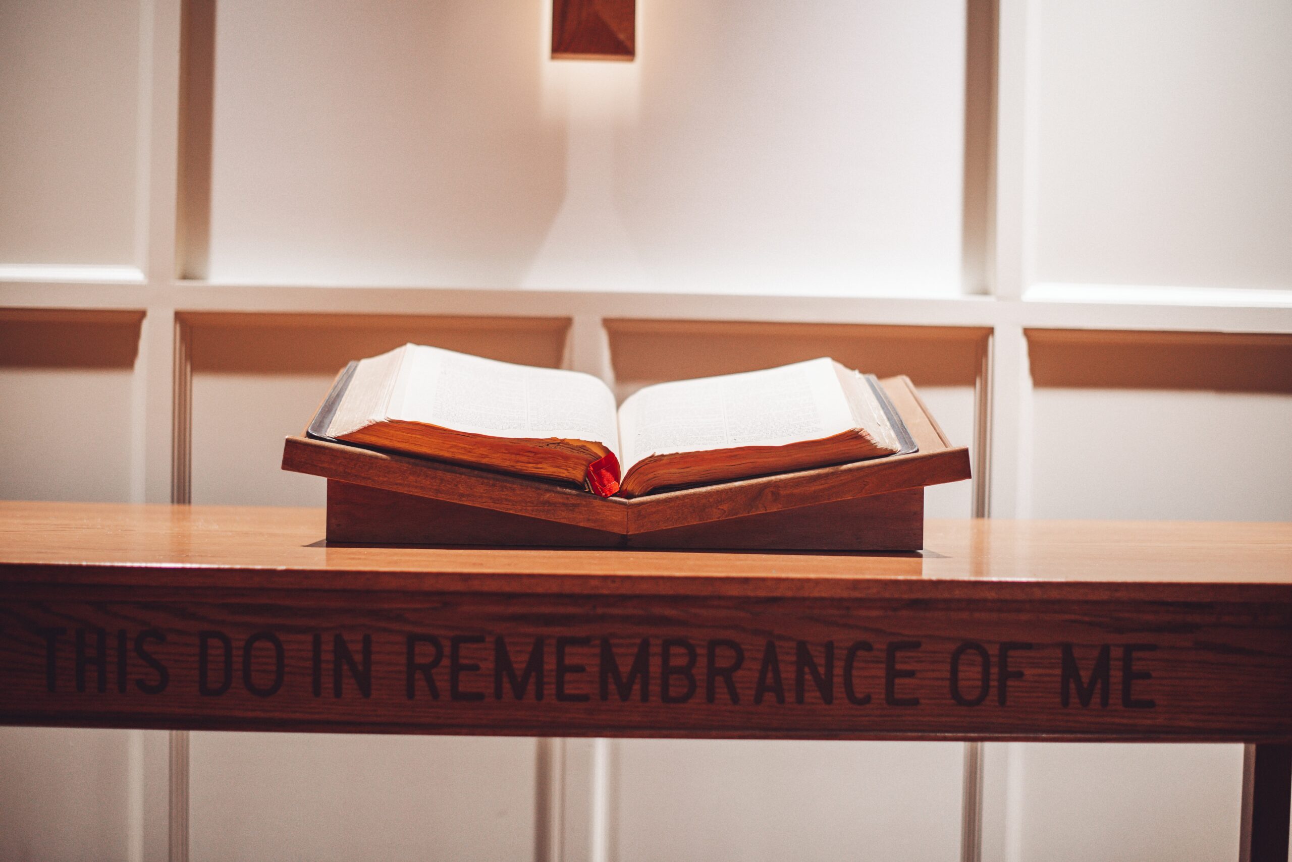 A picture of a Bible laid out on an altar. The phrase, "This do in remembrance of me," engraved in the wood.