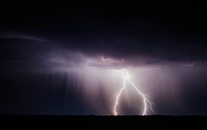 A picture of bright white lightning rods hitting the ground from the midst of dark storm clouds.
