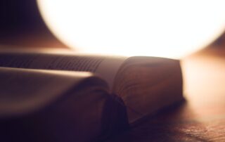 Close up of a BIble open on a table with a bright light beside it.