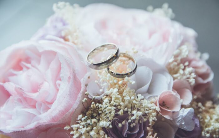 A picture of two gold wedding rings sitting on a pink floral bouquet.