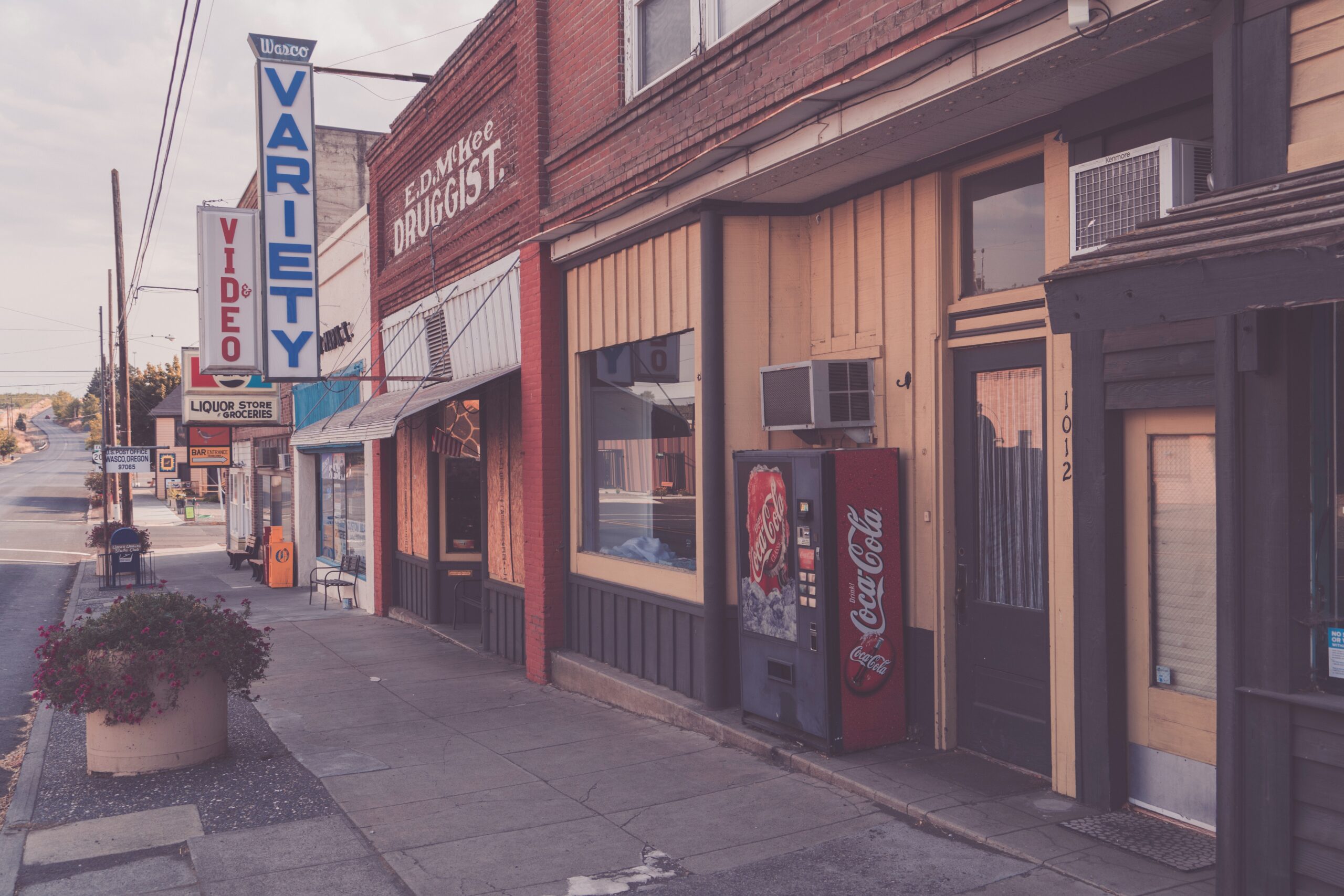 A picture of a main street with a drug store, a video store and a liquor store.