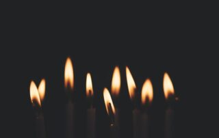 A picture of flames from candles grouped together in the midst of a dark room.