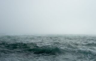 A picture from above a choppy, stormy sea with mist and clouds up above.