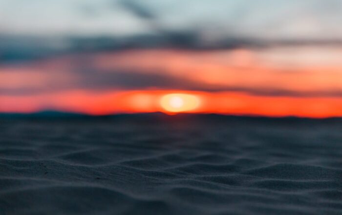 A close up of the sands on the beach with a bright orange sunset piercing the horizon in the distance.