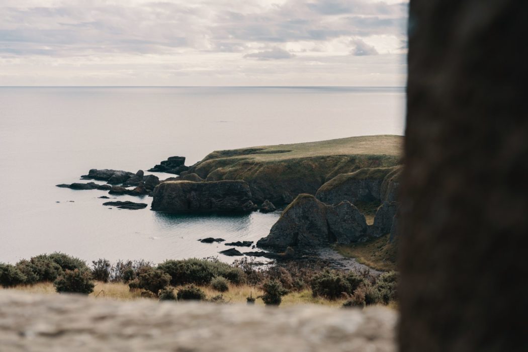 The view from above a grassy cliff beside the ocean.