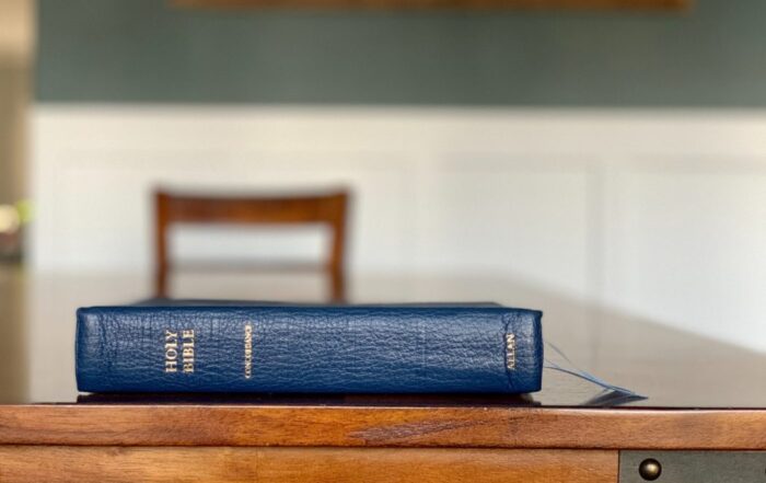Close up of the side of a blue Bible on a wooden table. The words "Holy Bible" are etched unto it.