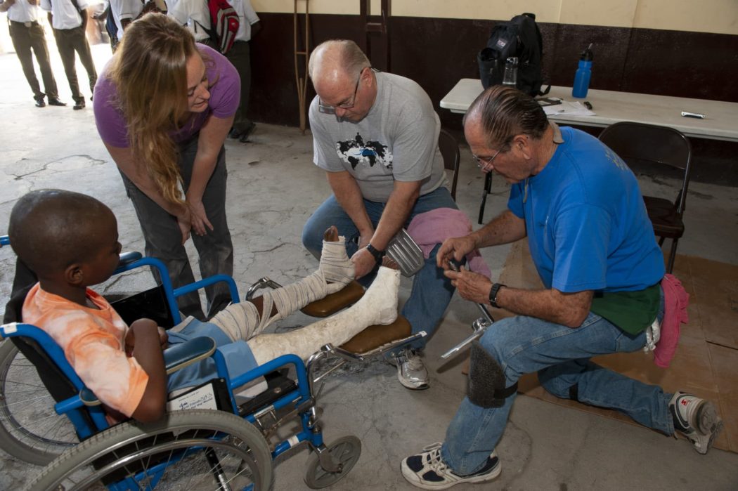 A picture of three Joni and Friends volunteers adjusting things on a little boy's wheelchair.