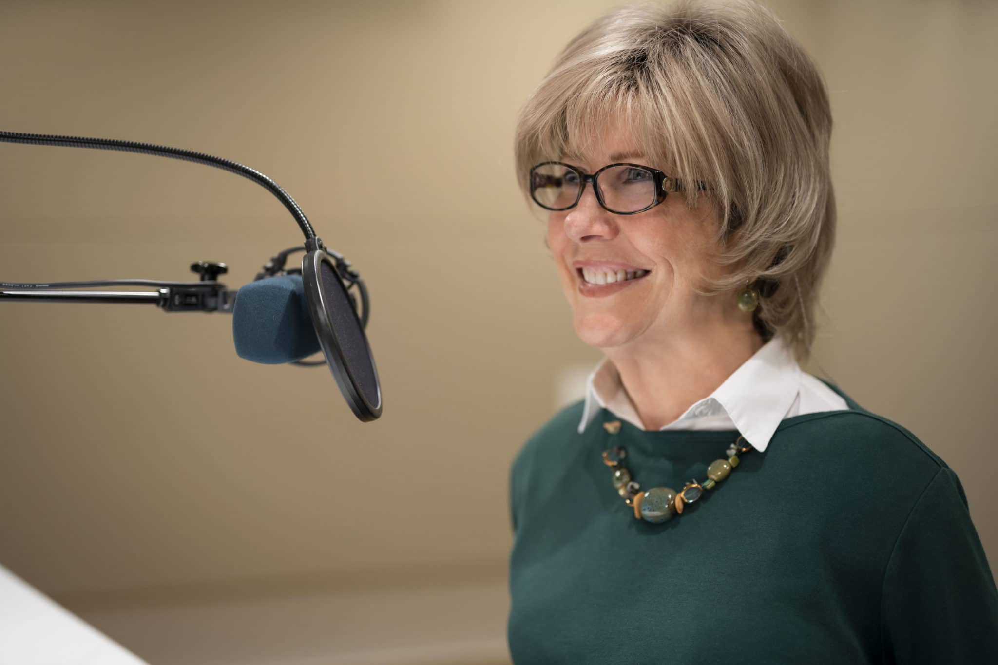 Close up of Joni in her thin-rimmed glasses smiling as she speaks into the radio microphone.