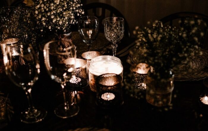 A picture of cups and candles on a table in a darkened room with baby's breath in a vase on the table.