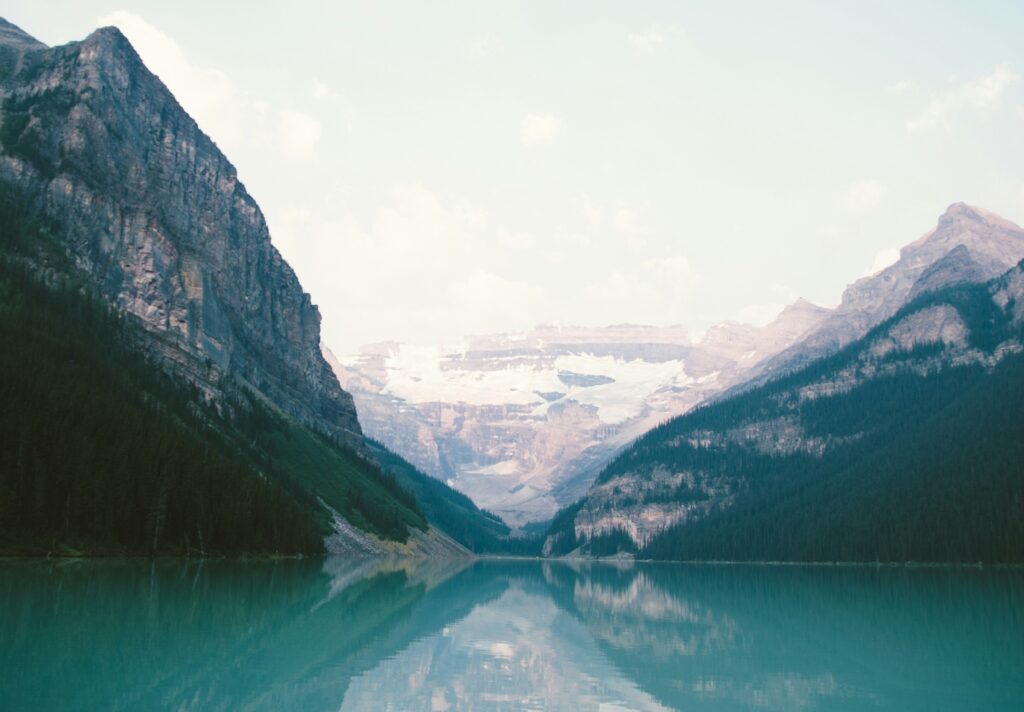A picture of mountains standing tall over a body of light blue water. The mountains are speckled with snow.