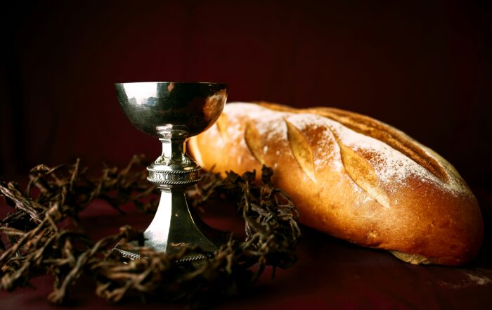 Close up of the communion elements on a table. On the table sits a loaf of French bread, a silver chalice, and a crown of thorns around the chalice.